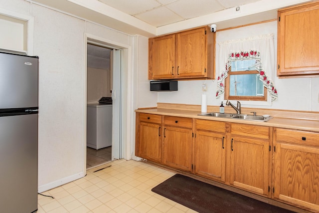 kitchen with freestanding refrigerator, washer / clothes dryer, a sink, light countertops, and brown cabinetry