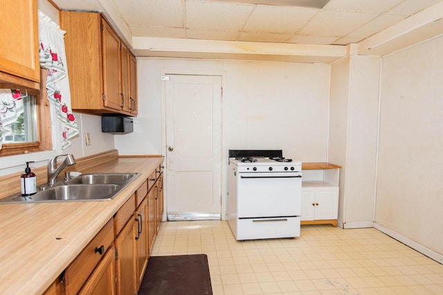 kitchen with white gas stove, a sink, light countertops, brown cabinetry, and a paneled ceiling