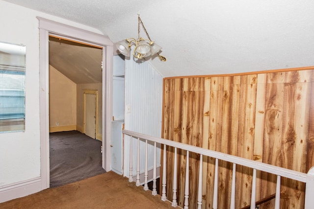 hallway with carpet flooring, a chandelier, lofted ceiling, and a textured ceiling