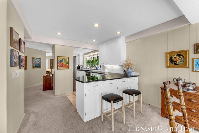kitchen featuring a peninsula, dark countertops, light carpet, white cabinetry, and recessed lighting
