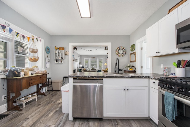 622 Thomas St SE, Grand Rapids, MI 49503 - kitchen featuring appliances with stainless steel finishes, dark countertops, a peninsula, a sink, and white cabinets