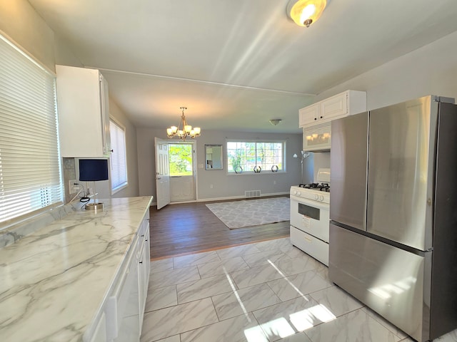 18453 Woodbine St, Detroit, MI 48219 - kitchen with freestanding refrigerator, white gas range oven, a chandelier, light marble finish floors, and white cabinets