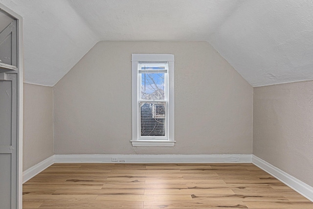 additional living space featuring light wood-type flooring, vaulted ceiling, baseboards, and a textured ceiling