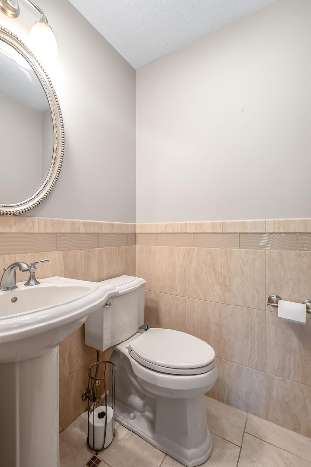 bathroom featuring tile patterned flooring, toilet, tile walls, a wainscoted wall, and a textured ceiling