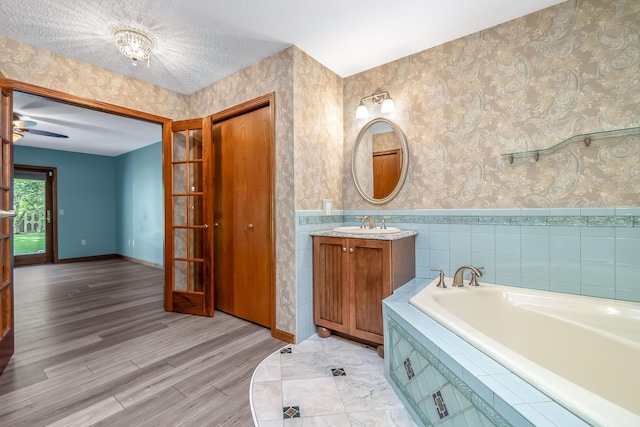 bathroom with a bath, vanity, wallpapered walls, and wood finished floors
