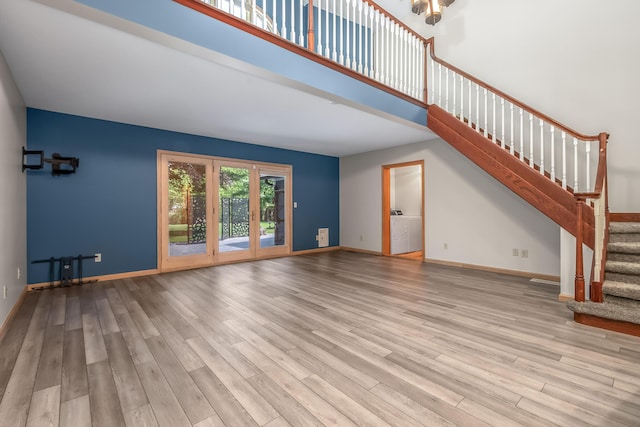 unfurnished living room with wood finished floors, stairway, baseboards, and a high ceiling