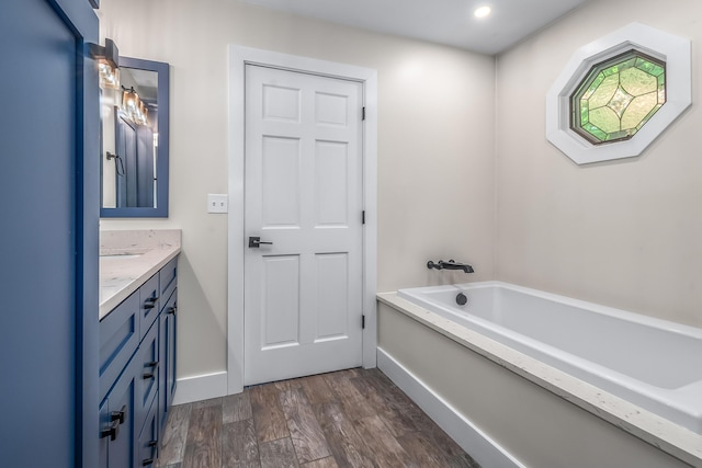 full bath with wood finished floors, vanity, a bath, baseboards, and recessed lighting