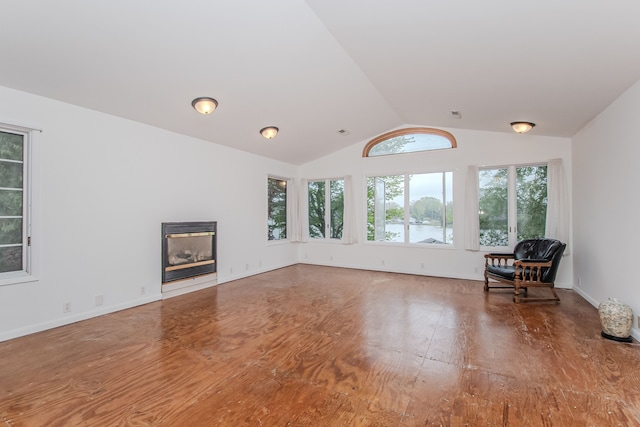 living room with wood finished floors, vaulted ceiling, a glass covered fireplace, and a water view