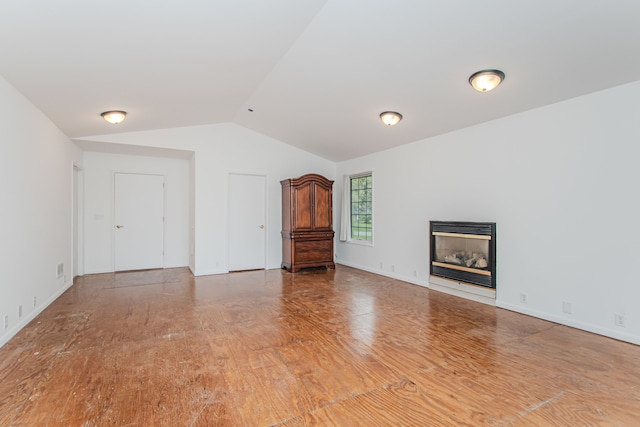 unfurnished living room featuring lofted ceiling, a glass covered fireplace, wood finished floors, and baseboards