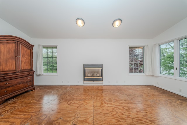 unfurnished living room featuring vaulted ceiling, baseboards, and a glass covered fireplace