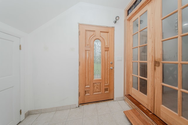 foyer featuring lofted ceiling, light tile patterned floors, and baseboards