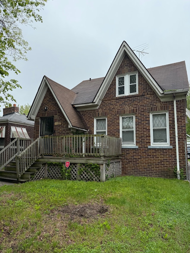 rear view of property with brick siding, a yard, and roof with shingles
