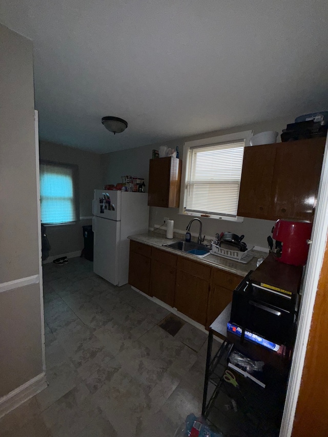 kitchen with a sink, freestanding refrigerator, brown cabinetry, light flooring, and light countertops