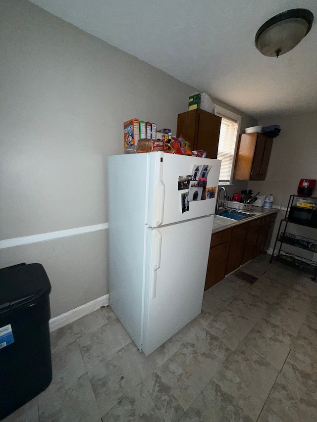 kitchen with freestanding refrigerator, a sink, light countertops, and brown cabinets