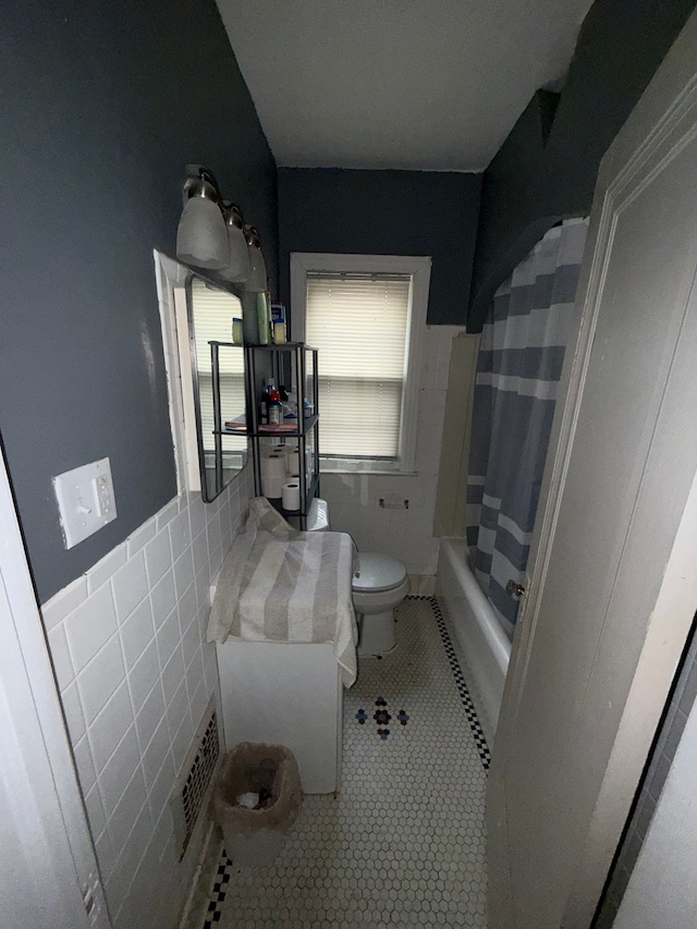 bathroom featuring toilet, tile patterned floors, tile walls, a wainscoted wall, and shower / bath combo