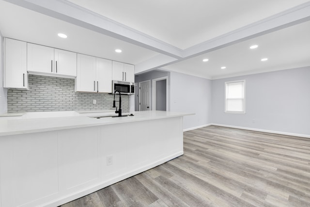 kitchen featuring a sink, baseboards, stainless steel microwave, backsplash, and white cabinetry