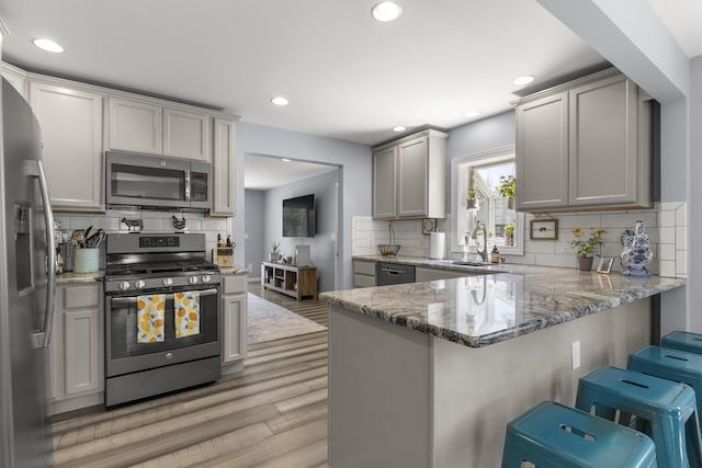 22171 Monterey Dr, Trenton, MI 48183 - kitchen featuring stainless steel appliances, a peninsula, light wood-style flooring, stone countertops, and decorative backsplash