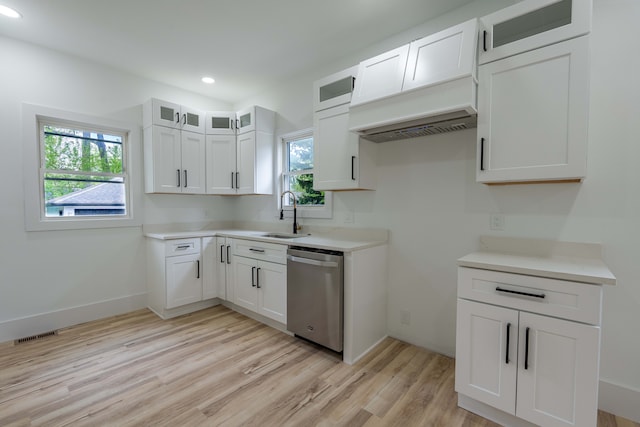 kitchen with stainless steel dishwasher, a sink, light wood-style flooring, white cabinetry, and glass insert cabinets