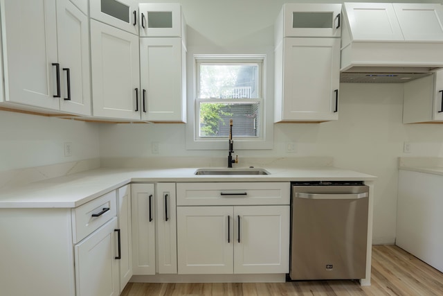 kitchen featuring stainless steel dishwasher, a sink, custom range hood, light wood-type flooring, and white cabinetry