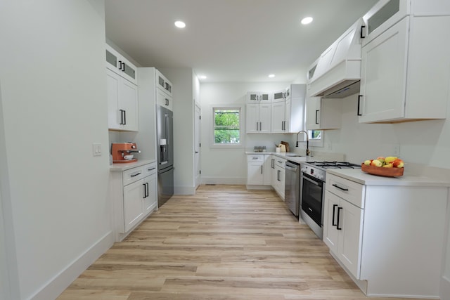 kitchen featuring appliances with stainless steel finishes, a sink, custom exhaust hood, light wood-style flooring, and light countertops