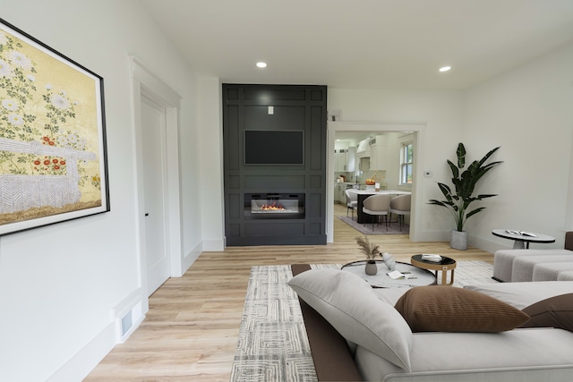 living room featuring a large fireplace, recessed lighting, light wood finished floors, and baseboards