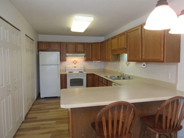 1303 Carriage Dr, Tecumseh, MI 49286 - kitchen featuring white appliances, under cabinet range hood, a sink, brown cabinetry, and a peninsula