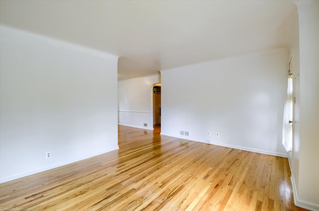 spare room with light wood finished floors, arched walkways, and baseboards