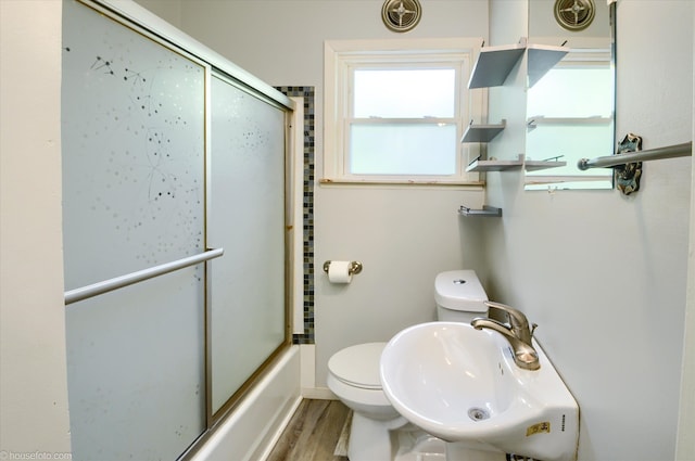 full bathroom with a sink, toilet, wood finished floors, and bath / shower combo with glass door