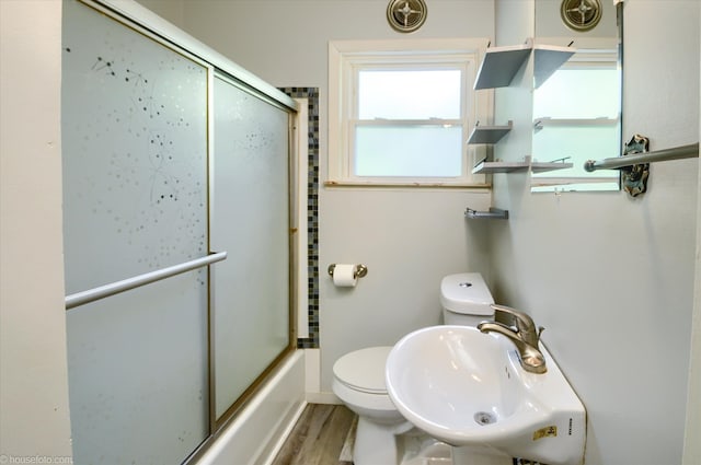 full bathroom with a sink, toilet, wood finished floors, and shower / bath combination with glass door
