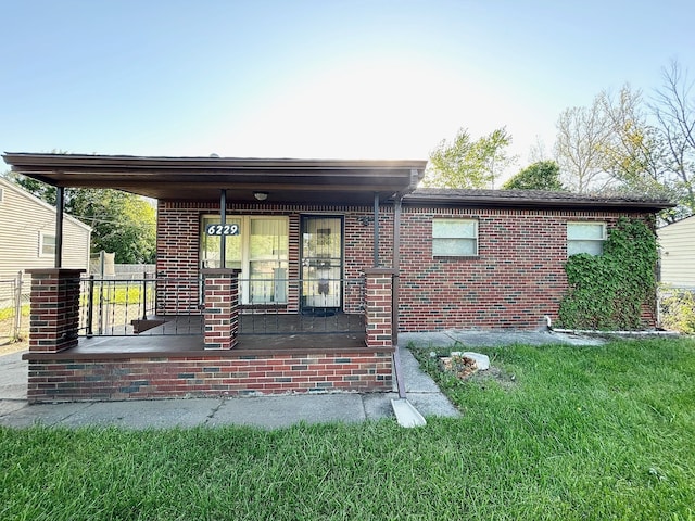 back of house with a porch, brick siding, and a lawn