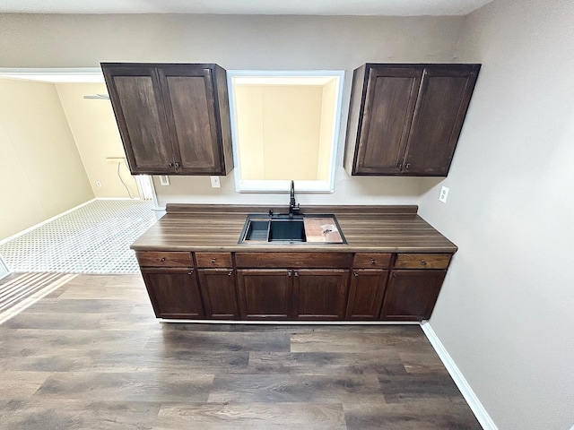 kitchen with a sink, dark wood-type flooring, dark brown cabinetry, and baseboards