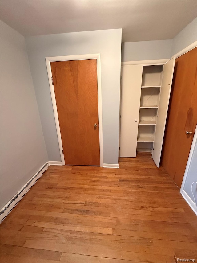 835 W Marr Rd, Howell, MI 48855 - unfurnished bedroom with a baseboard radiator, light wood-style flooring, a closet, and baseboards