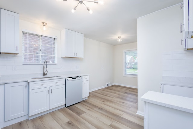 kitchen with white dishwasher, a sink, decorative backsplash, light wood finished floors, and white cabinets
