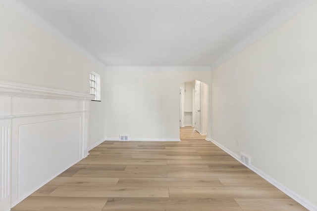 unfurnished room featuring light wood-style flooring, baseboards, and arched walkways