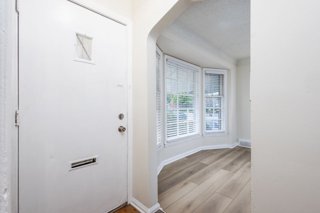 entrance foyer with light wood-style floors, a textured ceiling, baseboards, and arched walkways