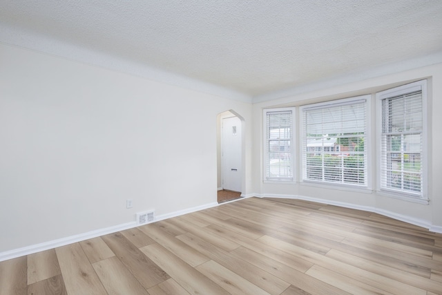 unfurnished room featuring arched walkways, light wood-type flooring, baseboards, and a textured ceiling