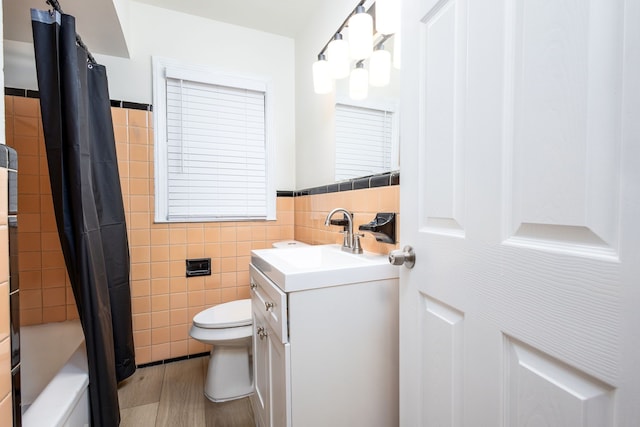 bathroom with tile walls, toilet, vanity, a wainscoted wall, and shower / bath combo with shower curtain
