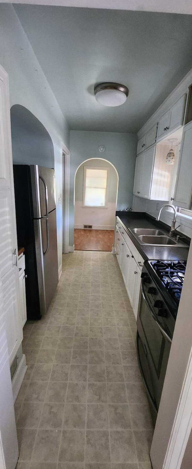 kitchen with a sink, appliances with stainless steel finishes, arched walkways, dark countertops, and healthy amount of natural light