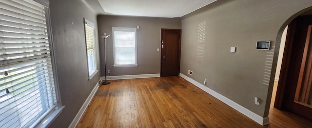 foyer with arched walkways, wood finished floors, and baseboards