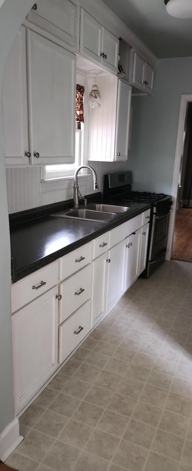 kitchen featuring gas stove, a sink, dark countertops, and white cabinetry