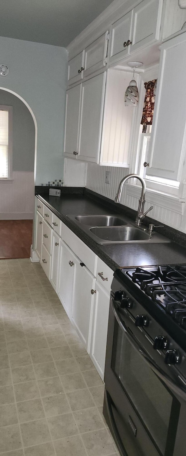 kitchen featuring black gas stove, a sink, white cabinets, dark countertops, and arched walkways