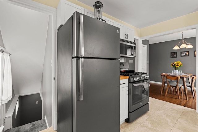 kitchen featuring appliances with stainless steel finishes, a chandelier, white cabinets, light tile patterned floors, and baseboards