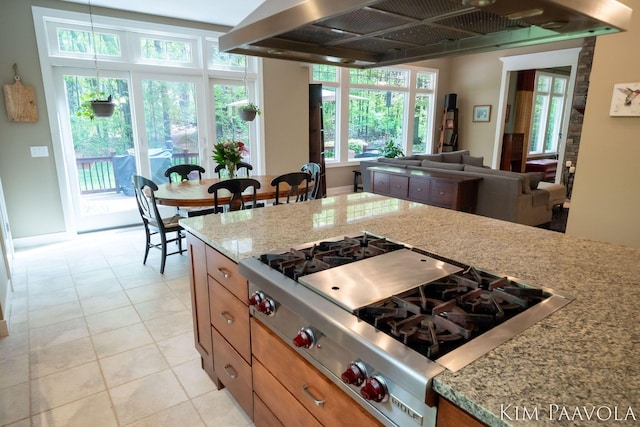 3099 Pickford Dr SE, Ada, MI 49301 - kitchen featuring stainless steel gas stovetop, ventilation hood, brown cabinetry, light stone countertops, and open floor plan