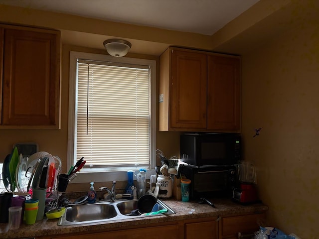 kitchen with black microwave, a sink, healthy amount of natural light, and brown cabinetry