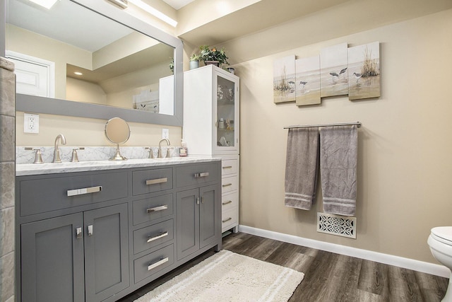 bathroom featuring wood finished floors, baseboards, double vanity, and toilet