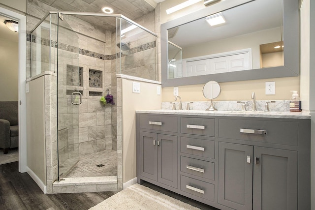 bathroom featuring wood finished floors, a stall shower, double vanity, and baseboards