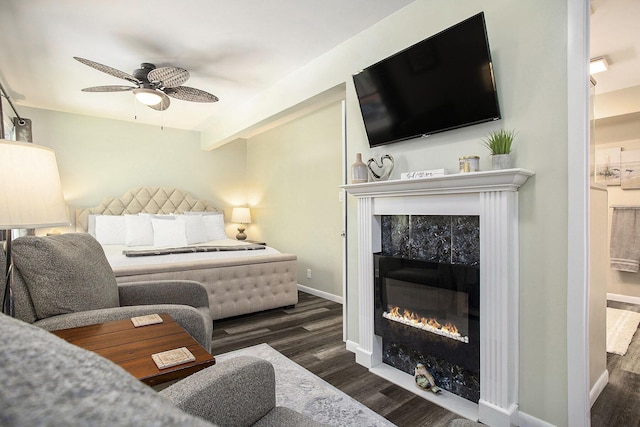 bedroom with a tiled fireplace, wood finished floors, baseboards, and ceiling fan
