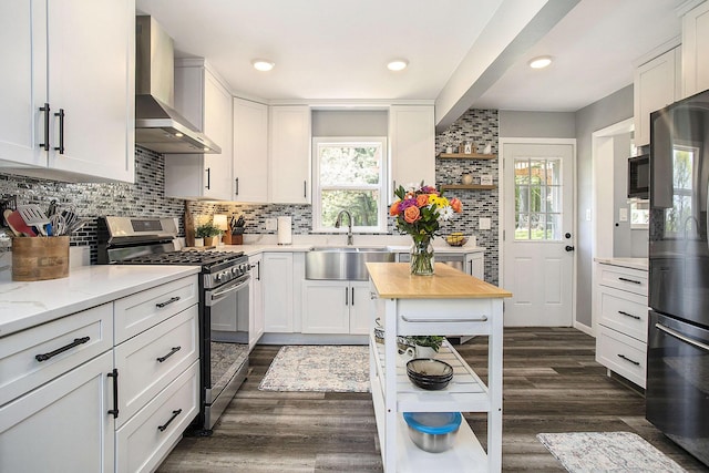kitchen featuring wall chimney exhaust hood, a sink, stainless steel gas range, freestanding refrigerator, and open shelves