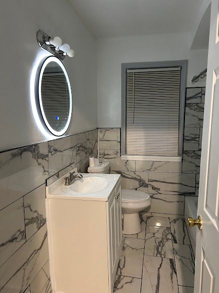 full bath featuring tile walls, vanity, toilet, marble finish flooring, and a tub