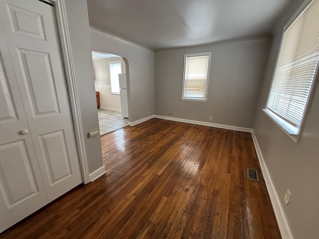 spare room with arched walkways, healthy amount of natural light, dark wood-style flooring, and baseboards